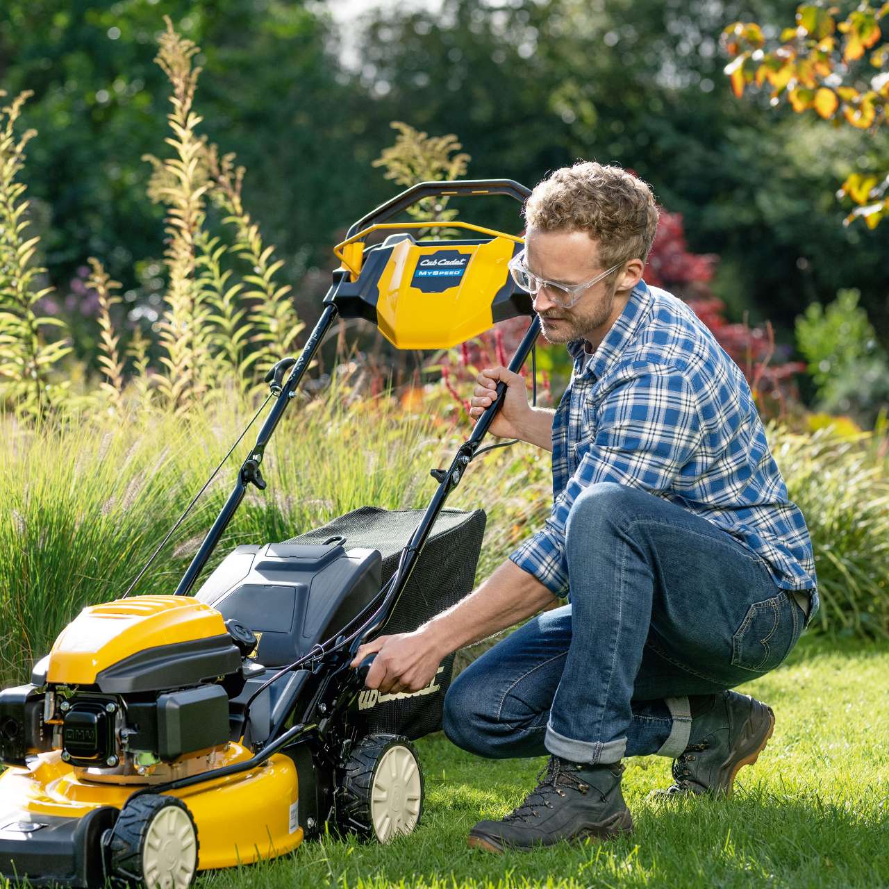 Mann im Garten bei der Einstellung eines Cub Cadet Benzin-Rasenmähers – sonnige Umgebung.