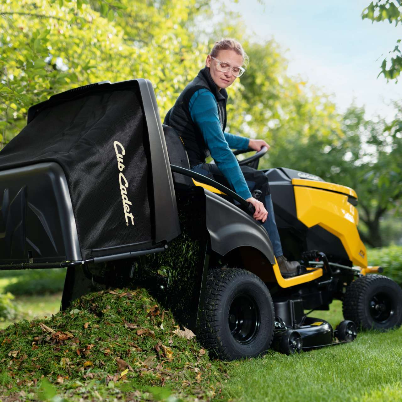 Person auf Cub Cadet Rasentraktor beim Entleeren des Fangsacks – Einsatz im grünen Gartenumfeld.